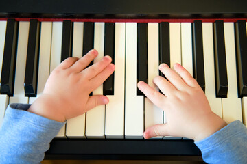 Toddler baby plays piano in home living room, music lessons. Happy child boy learns to play music on an electric piano. Kid boy age one year four months
