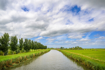 Typical Dutch river landscape with green meadows, canal and blue sky and clouds, Netherlands.
