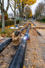 Soudure des tuyaux d'un r&eacute;seau de chaleur par un soudeur. Chauffage urbain, canalisations enterr&eacute;es. 