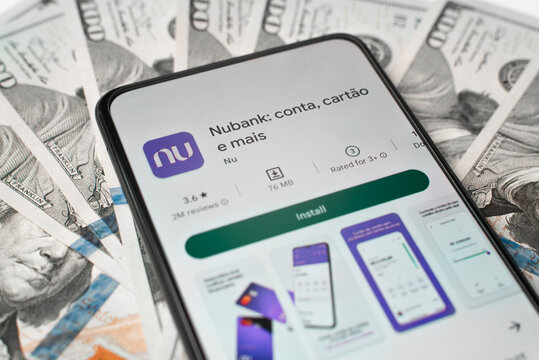 Nubank bank financial mobile application in online store Google Play on smartphone screen lying on money indoors, close-up. Astana, Kazakhstan 04.12.2022