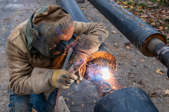Soudure des tuyaux d'un r&eacute;seau de chaleur par un soudeur. Chauffage urbain, canalisations enterr&eacute;es. 