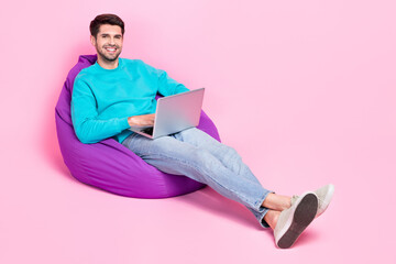 Full length photo of handsome young guy sit bean bag working remotely coder wear trendy blue clothes isolated on pink color background