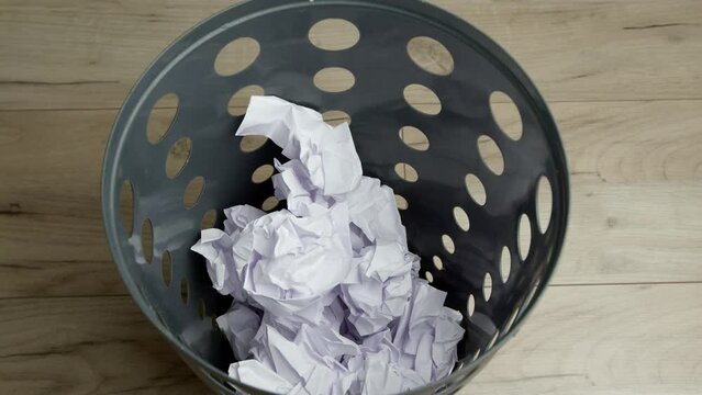 Crumpled office paper falls into the trash can.