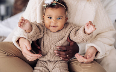 Hands of parents hold joyful mixed race baby girl.