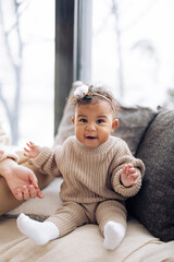 Fototapeta premium Happy mixed race baby girl sits near pillows against window.