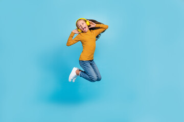 Full body photo of cheerful overjoyed girl jumping have fun hands touch headphones isolated on blue...