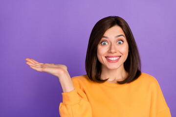 Closeup photo of young millennial cute pretty lady wear orange shirt toothy smile excited hold palm recommend promo product isolated on purple color background