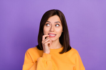Closeup photo of young pretty cute woman wear orange sweater bite nails nervous toothy look curious empty space ad isolated on purple color background