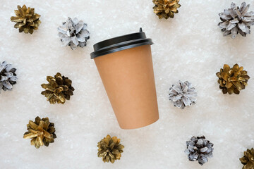 A paper cup of coffee to go with golden and white pine cones lies in the snow top view