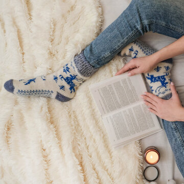 A girl in jeans and cozy socks reads a book in bed on a fluffy white bedspread top view
