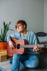  Woman with short hair enjoys playing guitar at home. Music lessons for adults