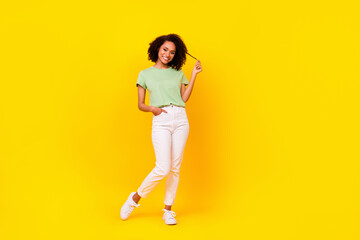 Fototapeta na wymiar Full size photo of young attractive pretty adorable gorgeous nice woman wear green t-shirt white pants touch curls advert empty space isolated on yellow color background
