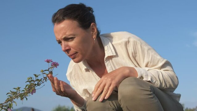 A woman smells a flower and scratches her nose. Allergy concept during flowering.