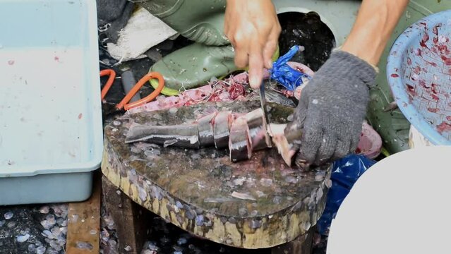 a seafood seller is cutting a customer's order of fish.