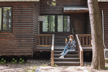 Young stylish caucasian woman 30-35 years old wearing casual clothing shirt and cowboy hat. Influencer using social media via mobile phone. Person enjoys life at morning during summer adventure in