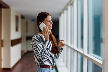 A woman with a phone in her hands talking and laughing while looking out the window at the city