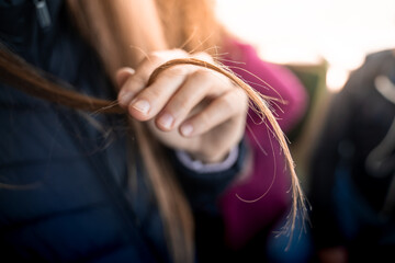 Close up of girl's hand showing split ends in hair. hair care and wellness concept.