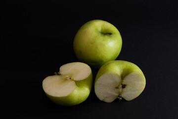 A Whole and a slice of apple on a black background, side view, Green apples, fresh, isolated on black, sliced apple on a stick