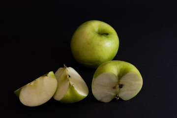 A Whole and a slice of apple on a black background, side view, Green apples, fresh, isolated on black, sliced apple on a stick