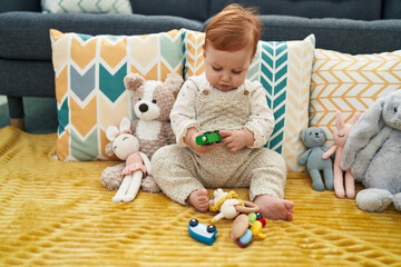 Naklejka premium Adorable redhead toddler playing with car toy sitting on sofa at home