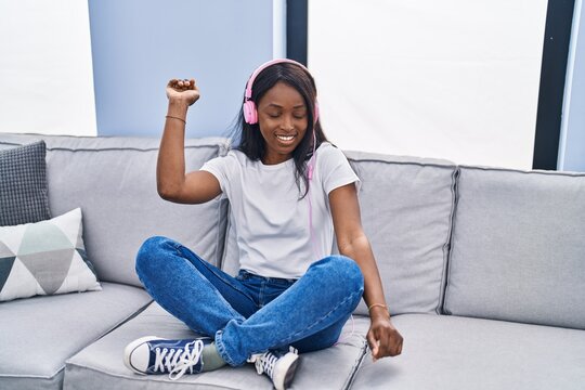 Young african american woman listening to music sitting on sofa at home