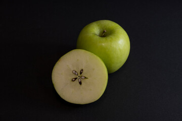 A Whole and a slice of apple on a black background, side view, Green apples, fresh, isolated on black, sliced apple on a stick