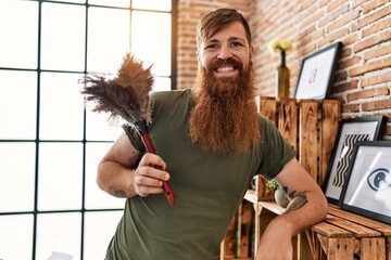 Young redhead man smiling confident cleaning dust at home