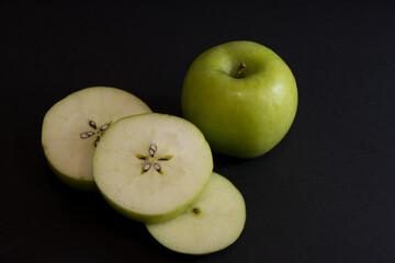 A Whole and a slice of apple on a black background, side view, Green apples, fresh, isolated on black, sliced apple on a stick