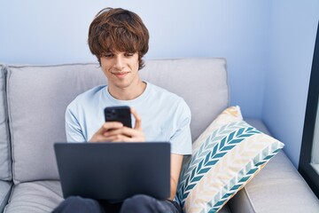 Young blond man using smartphone and laptop at home