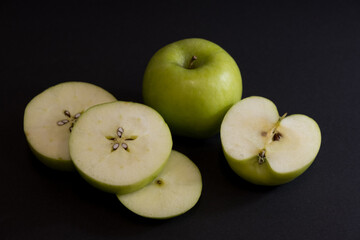 A Whole and a slice of apple on a black background, side view, Green apples, fresh, isolated on black, sliced apple on a stick