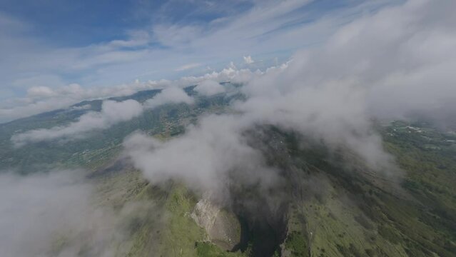 Volcano mountain with fog into crater surrounded by exotic greenery valley altitude natural aerial view. FPV sports drone dive close low shot volcanic scenery cliff canyon exotic island summit travel