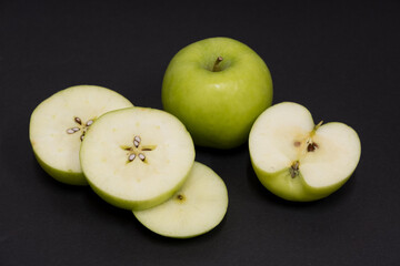 A Whole and a slice of apple on a black background, side view, Green apples, fresh, isolated on black, sliced apple on a stick