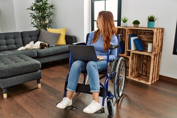 Young caucasian woman using laptop sitting on wheelchair at home