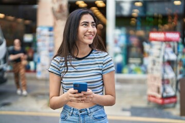 Young hispanic girl smiling confident using smartphone at street