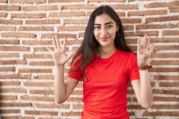 Young teenager girl standing over bricks wall showing and pointing up with fingers number nine...