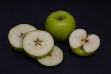 A Whole and a slice of apple on a black background, side view, Green apples, fresh, isolated on black, sliced apple on a stick