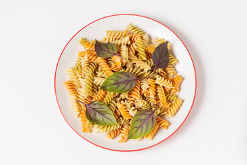 Spiral colored fusilli pasta with fresh basil in a plate isolated on white background top view