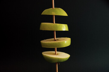 A Whole and a slice of apple on a black background, side view, Green apples, fresh, isolated on black, sliced apple on a stick
