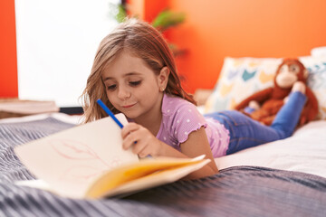 Adorable hispanic girl writing on notebook lying on bed at bedroom
