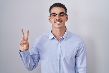 Handsome hispanic man wearing business clothes and glasses showing and pointing up with fingers number two while smiling confident and happy.