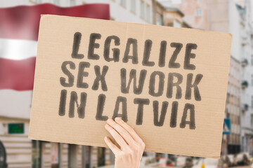 The phrase " Legalize Sex Work in Latvia " is on a banner in men's hands with blurred background. Guide. Govern. Body. Coworker. Crime. Criminal. Democracy. Desire. Employee. Earnings. Dollars