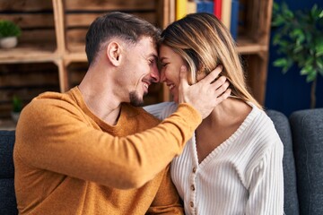 Young man and woman couple hugging each other sitting on sofa at home