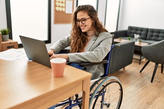 Young beautiful hispanic woman business worker using laptop sitting on wheelchair at office