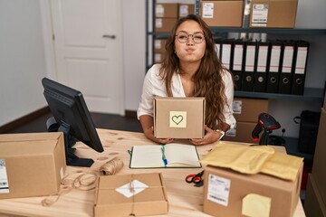 Young hispanic woman working at small business ecommerce puffing cheeks with funny face. mouth inflated with air, catching air.
