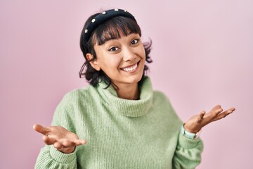 Young beautiful woman standing over pink background smiling cheerful with open arms as friendly welcome, positive and confident greetings