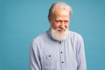 Portrait of white beard old man wear light blue shirt on blue color background - positive human...