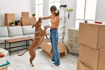 Young caucasian woman listening to music feeding dog at home