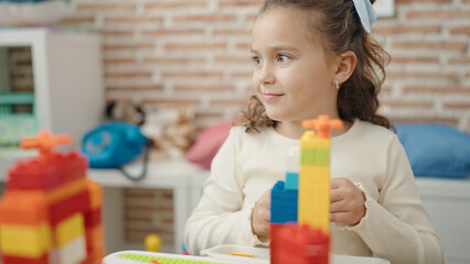 Adorable caucasian girl playing with construction blocks sitting on table at kindergarten
