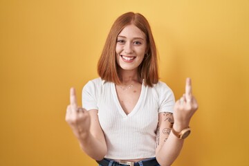 Young redhead woman standing over yellow background showing middle finger doing fuck you bad...