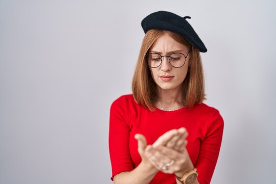 Young redhead woman standing wearing glasses and beret suffering pain on hands and fingers, arthritis inflammation
